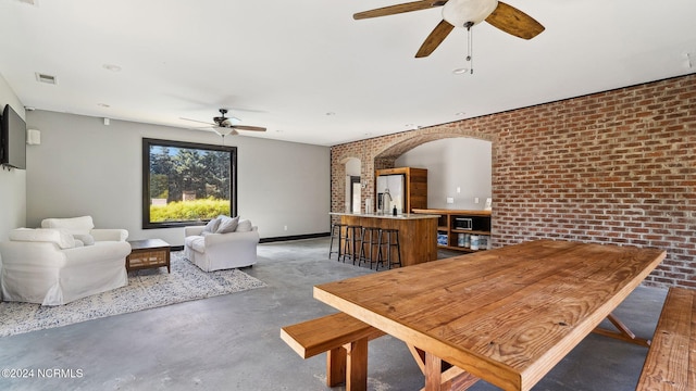 dining area with a ceiling fan, concrete floors, brick wall, and visible vents