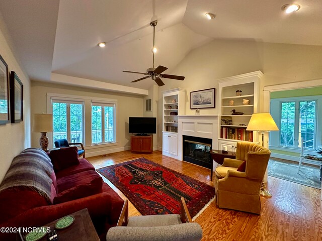 living room featuring light hardwood / wood-style floors, vaulted ceiling, ceiling fan, and built in features