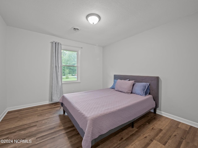 bedroom featuring a textured ceiling and dark hardwood / wood-style flooring