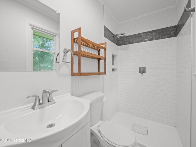 bathroom featuring ornamental molding, vanity, a tile shower, and toilet