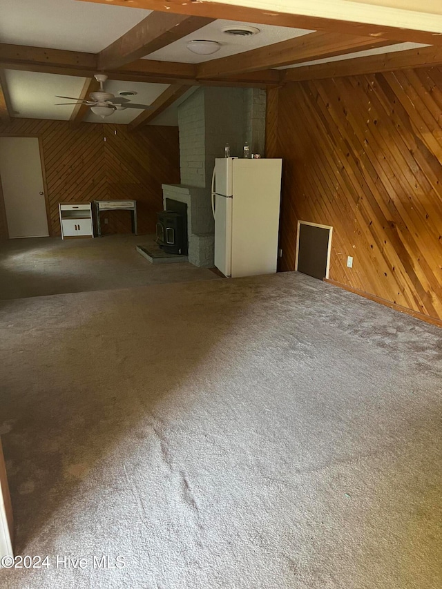 unfurnished living room with beamed ceiling, wooden walls, and a wood stove