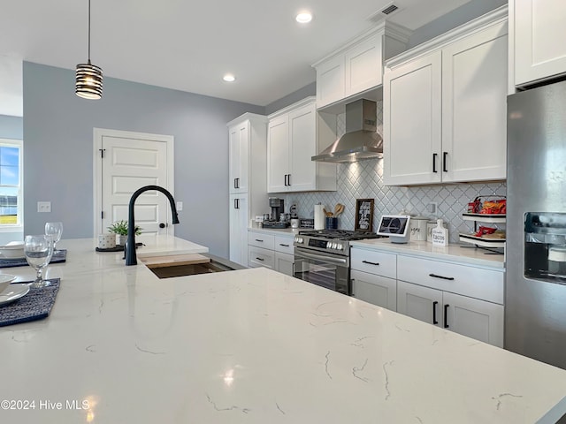 kitchen featuring appliances with stainless steel finishes, light stone counters, sink, wall chimney range hood, and pendant lighting