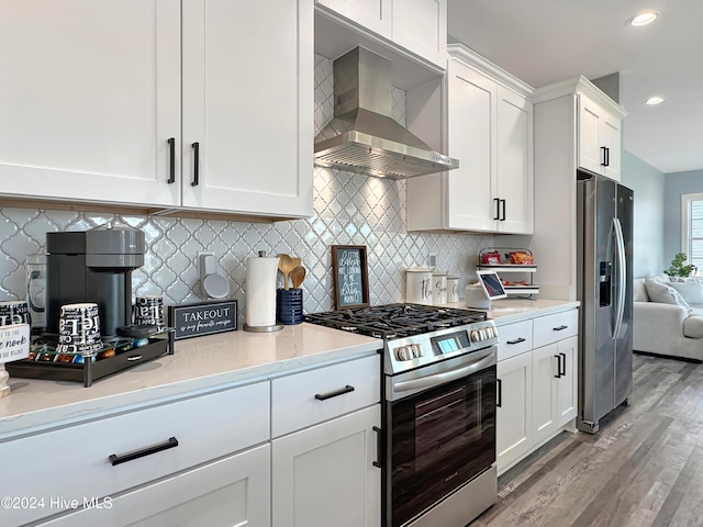 kitchen featuring appliances with stainless steel finishes, light wood-type flooring, tasteful backsplash, wall chimney exhaust hood, and white cabinetry