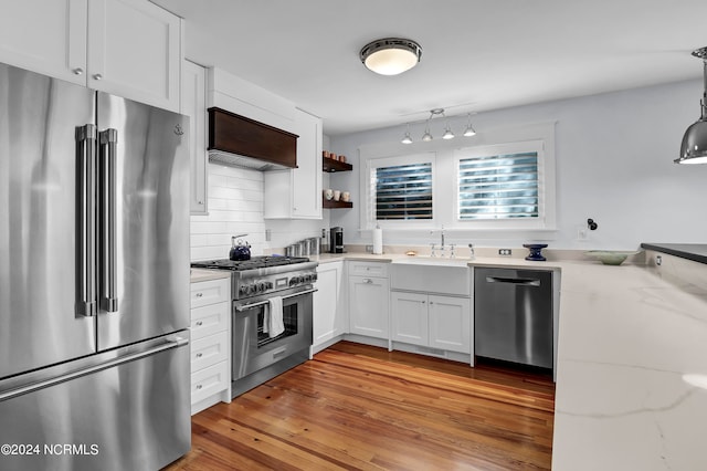 kitchen with hanging light fixtures, light hardwood / wood-style floors, white cabinetry, premium appliances, and light stone countertops