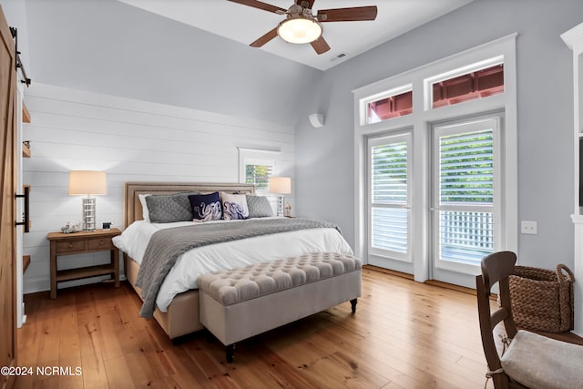 bedroom featuring ceiling fan, wood walls, wood-type flooring, a barn door, and access to exterior