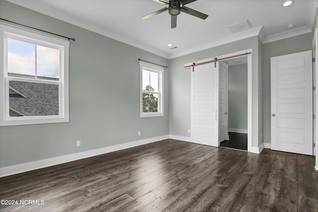 unfurnished bedroom with ornamental molding, ceiling fan, a barn door, dark wood-type flooring, and a closet