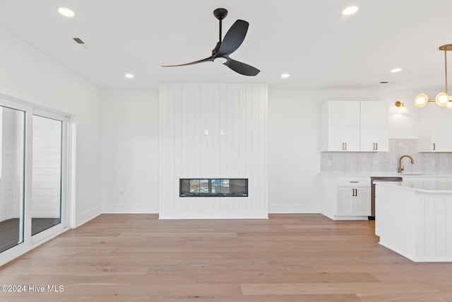 unfurnished living room with a fireplace, ceiling fan, light wood-type flooring, and sink