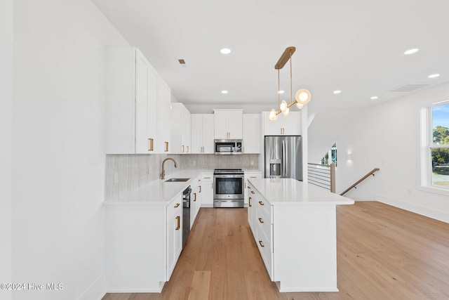 kitchen with appliances with stainless steel finishes, sink, pendant lighting, white cabinets, and a kitchen island