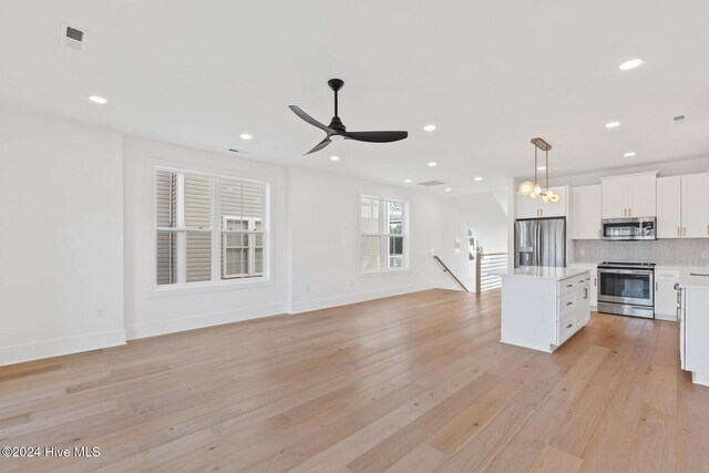 kitchen with appliances with stainless steel finishes, tasteful backsplash, white cabinets, a kitchen island, and hanging light fixtures