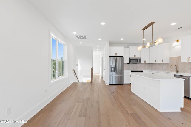 kitchen featuring white cabinetry, backsplash, pendant lighting, a kitchen island, and appliances with stainless steel finishes