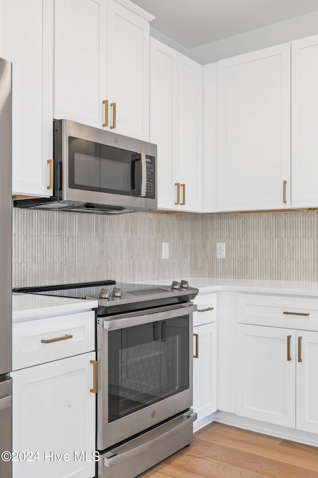 kitchen with white cabinets, appliances with stainless steel finishes, light wood-type flooring, and backsplash