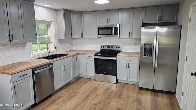 kitchen with appliances with stainless steel finishes, tasteful backsplash, wooden counters, light wood-type flooring, and sink