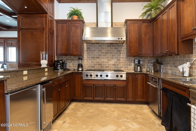 kitchen featuring stainless steel appliances, tasteful backsplash, sink, dark stone counters, and wall chimney range hood