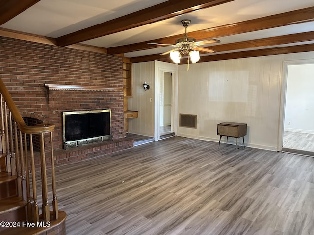 unfurnished living room with ceiling fan, a fireplace, beamed ceiling, and wood-type flooring