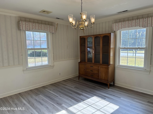 unfurnished dining area with hardwood / wood-style flooring, ornamental molding, a wealth of natural light, and an inviting chandelier