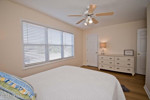 bedroom with a textured ceiling, ceiling fan, and dark hardwood / wood-style floors