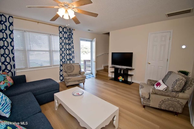 living room featuring ceiling fan, a textured ceiling, and light wood-type flooring