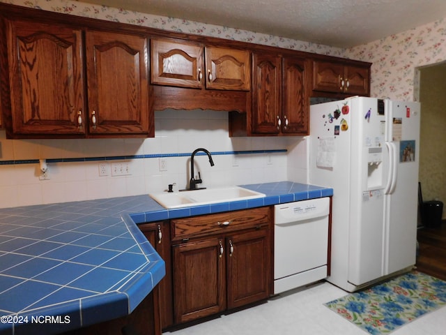 kitchen featuring sink, white appliances, a textured ceiling, tile counters, and decorative backsplash