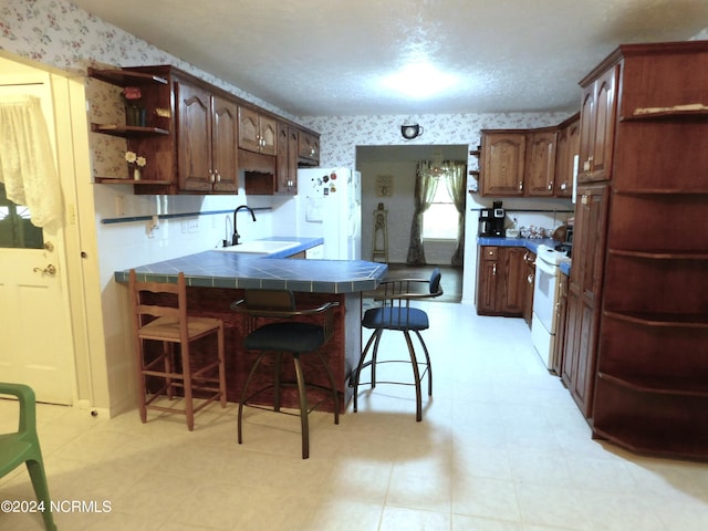 kitchen with sink, kitchen peninsula, white appliances, tile counters, and a kitchen bar