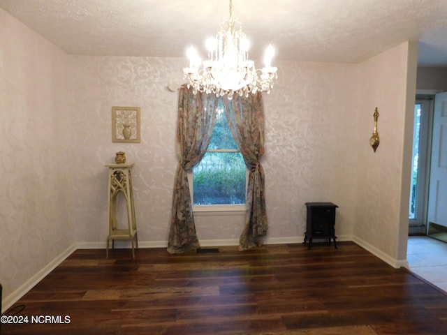 empty room featuring a textured ceiling, an inviting chandelier, and dark wood-type flooring