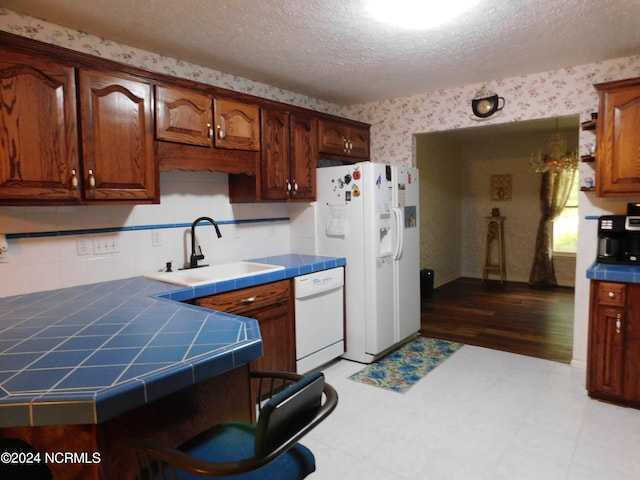 kitchen featuring light wood-type flooring, a textured ceiling, sink, white appliances, and tile countertops