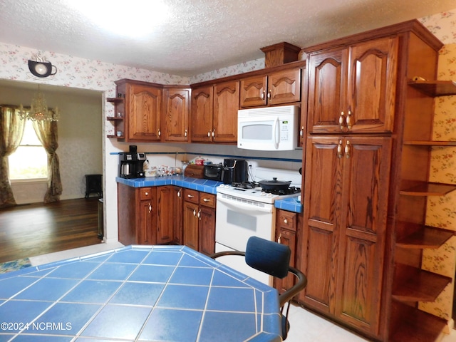 kitchen with a textured ceiling, white appliances, light hardwood / wood-style floors, and tile countertops