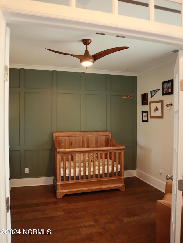 bedroom with dark wood-type flooring, ceiling fan, ornamental molding, and a crib