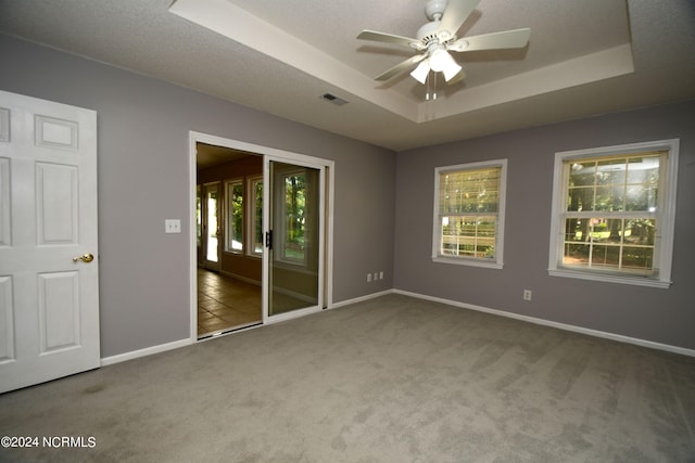 unfurnished bedroom with multiple windows, carpet flooring, a tray ceiling, and ceiling fan