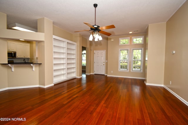 unfurnished living room with ceiling fan, a textured ceiling, dark wood-type flooring, and built in shelves