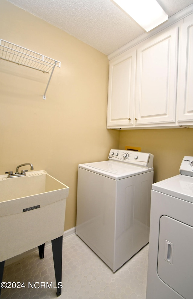 washroom featuring washing machine and clothes dryer, a textured ceiling, cabinets, and sink