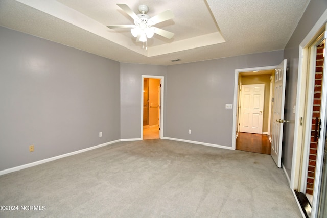 unfurnished bedroom featuring a textured ceiling, a tray ceiling, ceiling fan, and light colored carpet