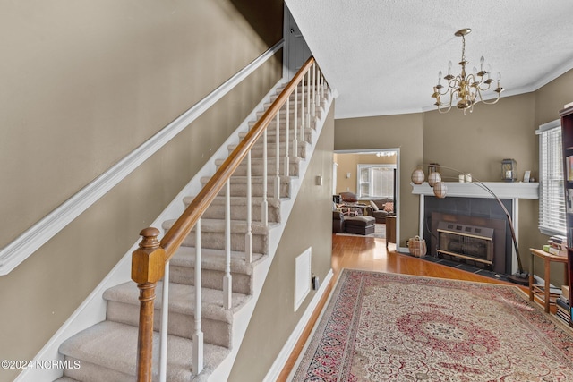 stairway with a chandelier, wood-type flooring, a textured ceiling, and crown molding