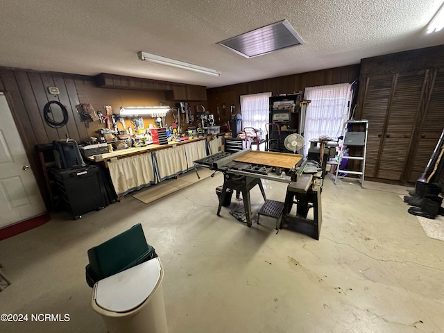 miscellaneous room featuring a workshop area, a textured ceiling, and wooden walls