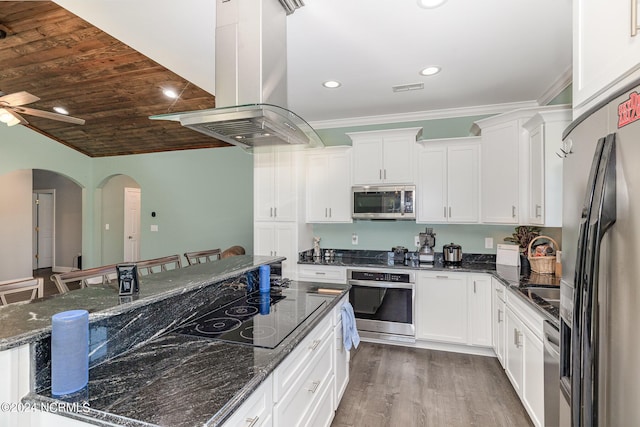 kitchen featuring island exhaust hood, appliances with stainless steel finishes, dark stone counters, white cabinets, and a breakfast bar area