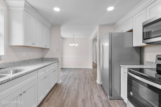 kitchen with white cabinetry, sink, stainless steel appliances, a notable chandelier, and light wood-type flooring