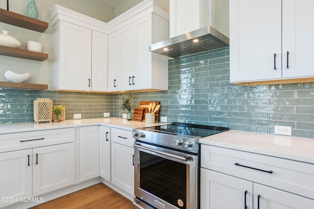 kitchen featuring white cabinets, wall chimney range hood, decorative backsplash, stainless steel electric range oven, and light hardwood / wood-style floors