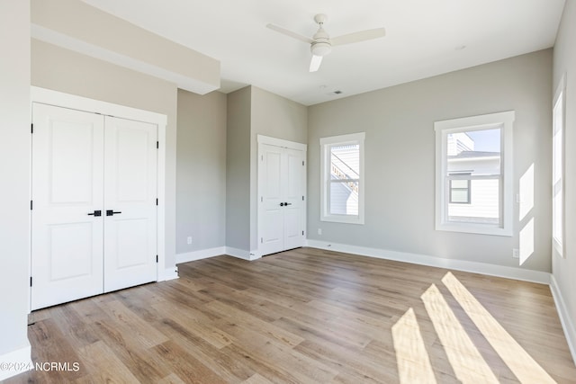 unfurnished bedroom with multiple windows, ceiling fan, two closets, and light hardwood / wood-style floors