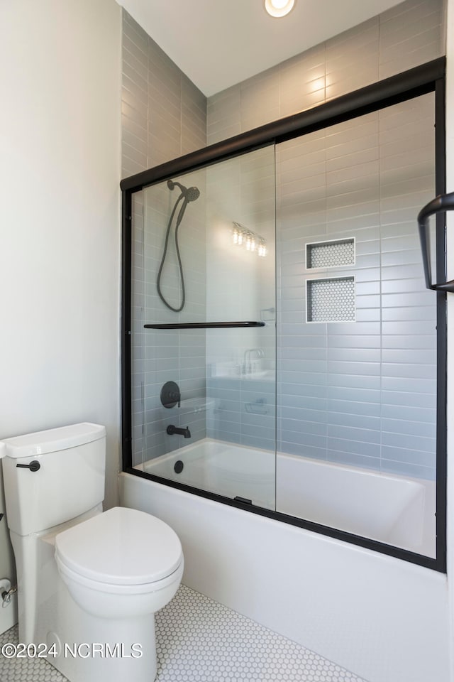 bathroom featuring tile patterned flooring, bath / shower combo with glass door, and toilet