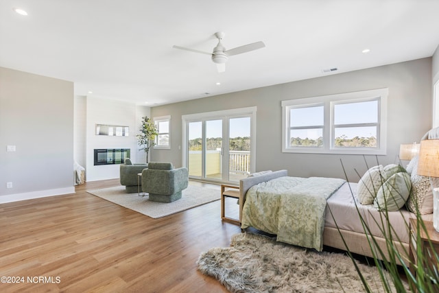 bedroom with a large fireplace, access to exterior, ceiling fan, and light hardwood / wood-style flooring