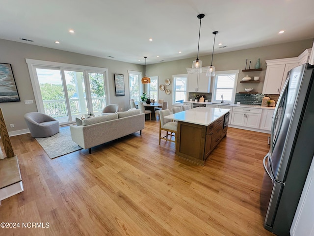 kitchen with white cabinetry, light hardwood / wood-style flooring, stainless steel fridge, a kitchen island, and decorative backsplash