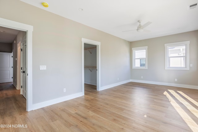 unfurnished bedroom featuring a walk in closet, ceiling fan, a closet, and light wood-type flooring