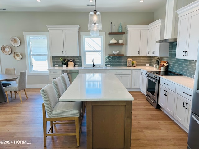 kitchen with pendant lighting, sink, stainless steel appliances, white cabinets, and a kitchen island