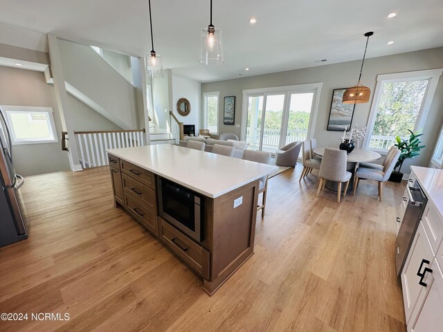 kitchen featuring stainless steel appliances, white cabinetry, hanging light fixtures, and light hardwood / wood-style floors