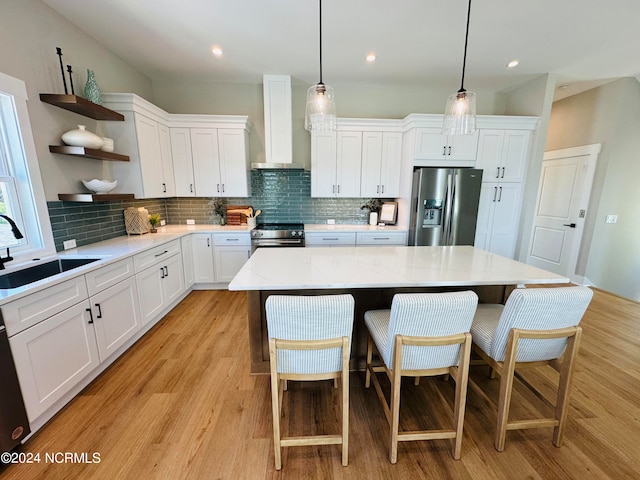 kitchen with pendant lighting, sink, stainless steel appliances, a kitchen island, and wall chimney exhaust hood