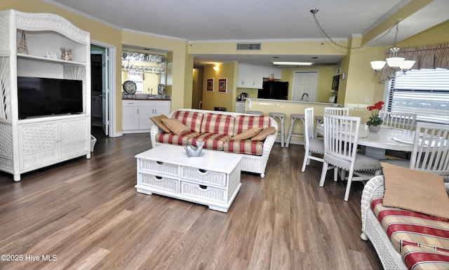 living area featuring dark wood-style floors, ornamental molding, visible vents, and an inviting chandelier