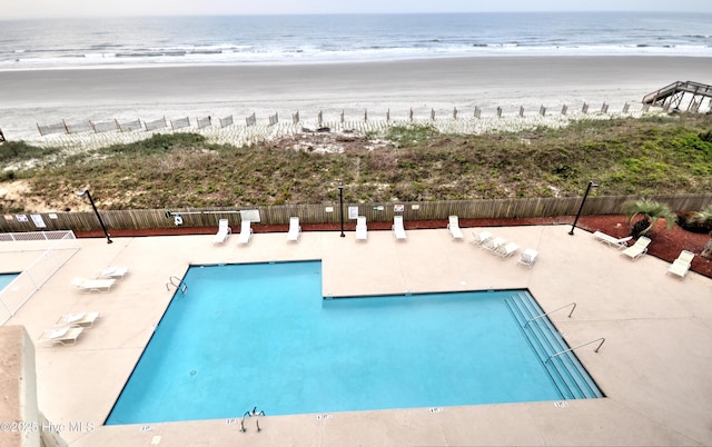 view of pool featuring a view of the beach, a water view, and fence