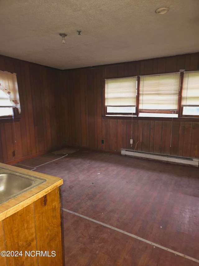 empty room featuring a baseboard radiator, wooden walls, dark hardwood / wood-style floors, and plenty of natural light