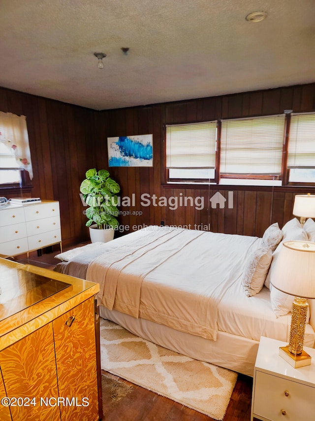 bedroom with a textured ceiling, wood walls, and dark wood-type flooring