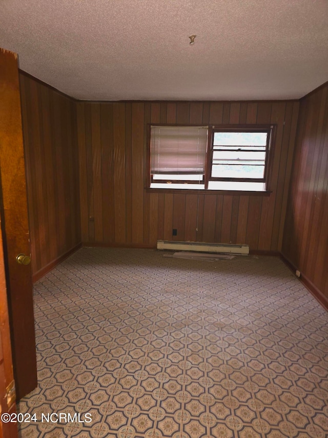 spare room with a textured ceiling, baseboard heating, and wood walls