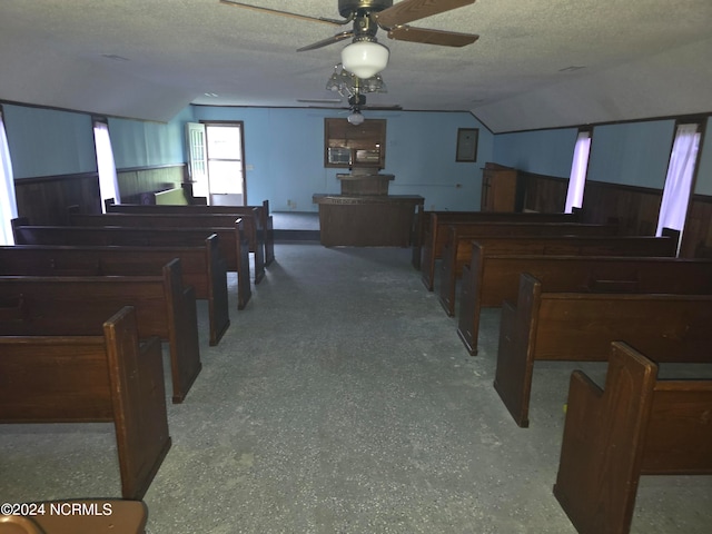 interior space featuring ceiling fan, a textured ceiling, wooden walls, and vaulted ceiling